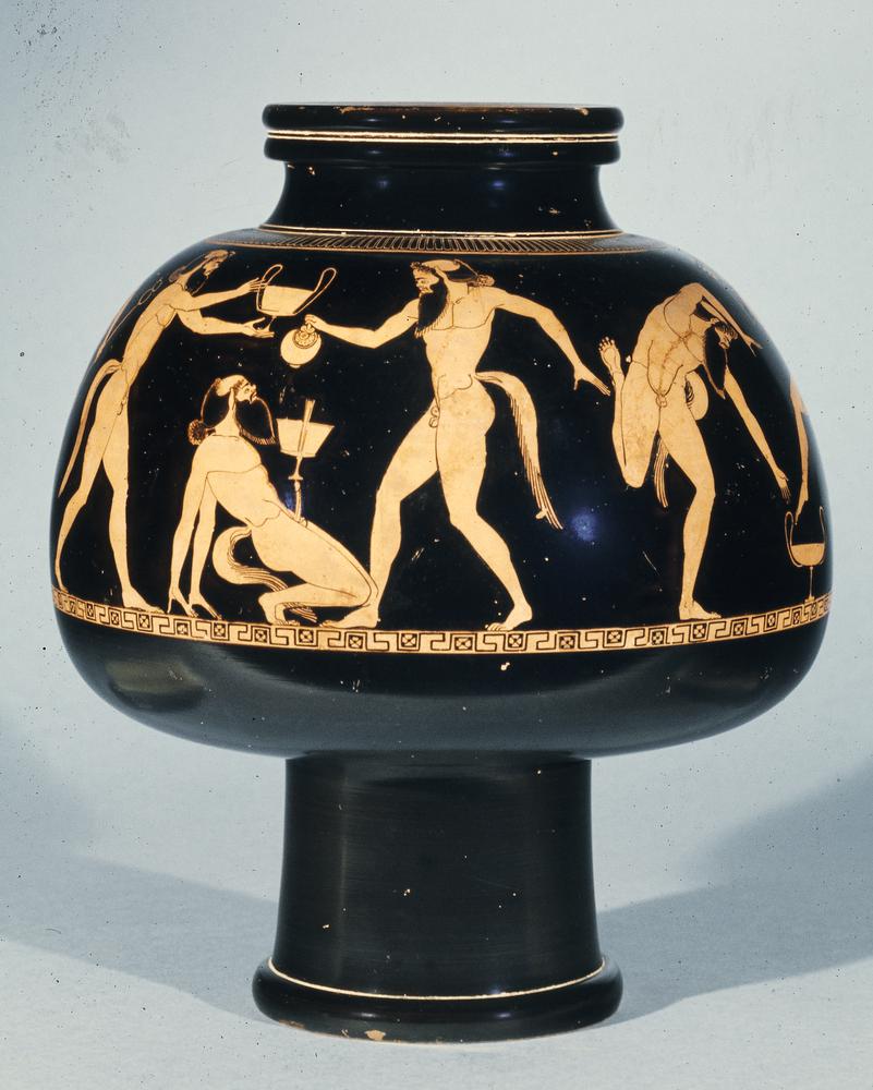 Four nude satyrs engage in drinking and revelry. One leans back on his hands, balancing a cantharos on his erect phallus. One pours wine into the cantharos; another stands behind him, holding a cantharos overhead. To the right, the fourth satyr dances around another cantharos, set on the ground.